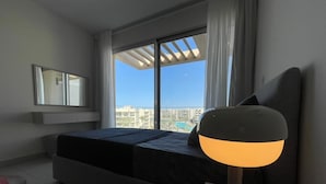 Une chambre d’hôtel moderne équipée d’un lit, d’un bureau, d’une chaise, d’une lampe et d’une grande fenêtre donnant sur la ville.