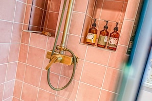 Une douche équipée d’un pommeau de douche à main, d’un tuyau flexible et d’un distributeur de savon fixé au mur.
