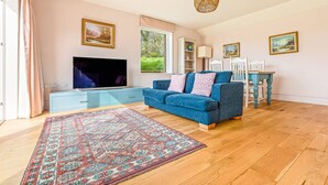 A living room with a blue sofa, a TV, a patterned rug, and a dining area with a table and chairs. - The Old Chicken Shed (Stoke Row)