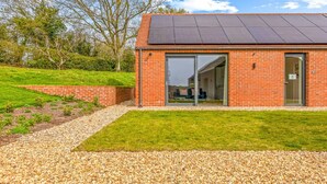 A modern building with a brick exterior, large glass doors, and a solar panel roof. - The Old Chicken Shed (Stoke Row)