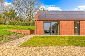 Un bâtiment moderne avec une façade en briques, de grandes portes vitrées et un toit recouvert de panneaux solaires.