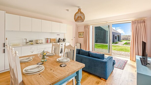 A modern kitchen with white cabinets, a dining table set for four, and a blue sofa in the living area. - The Old Chicken Shed (Stoke Row)