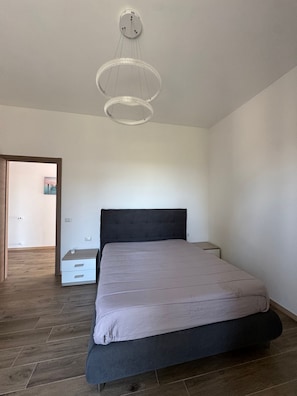 Un dormitorio con cama, mesitas de noche, una lámpara de araña moderna y suelo de madera.