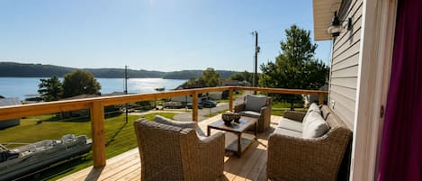 A wooden deck with wicker furniture, overlooking a body of water and a residential area.