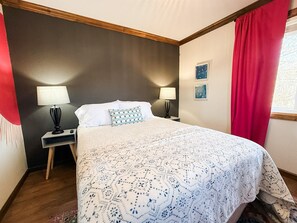 A bedroom with a bed, two bedside lamps, a nightstand, a red curtain, and two framed pictures on the wall. - Pink Pearl-Beaver Lake Views-Hot Tub-Sauna (Rogers)