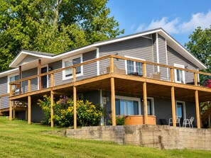 Une maison à deux étages dotée d’une terrasse en bois et d’un mur de soutènement en pierre.
