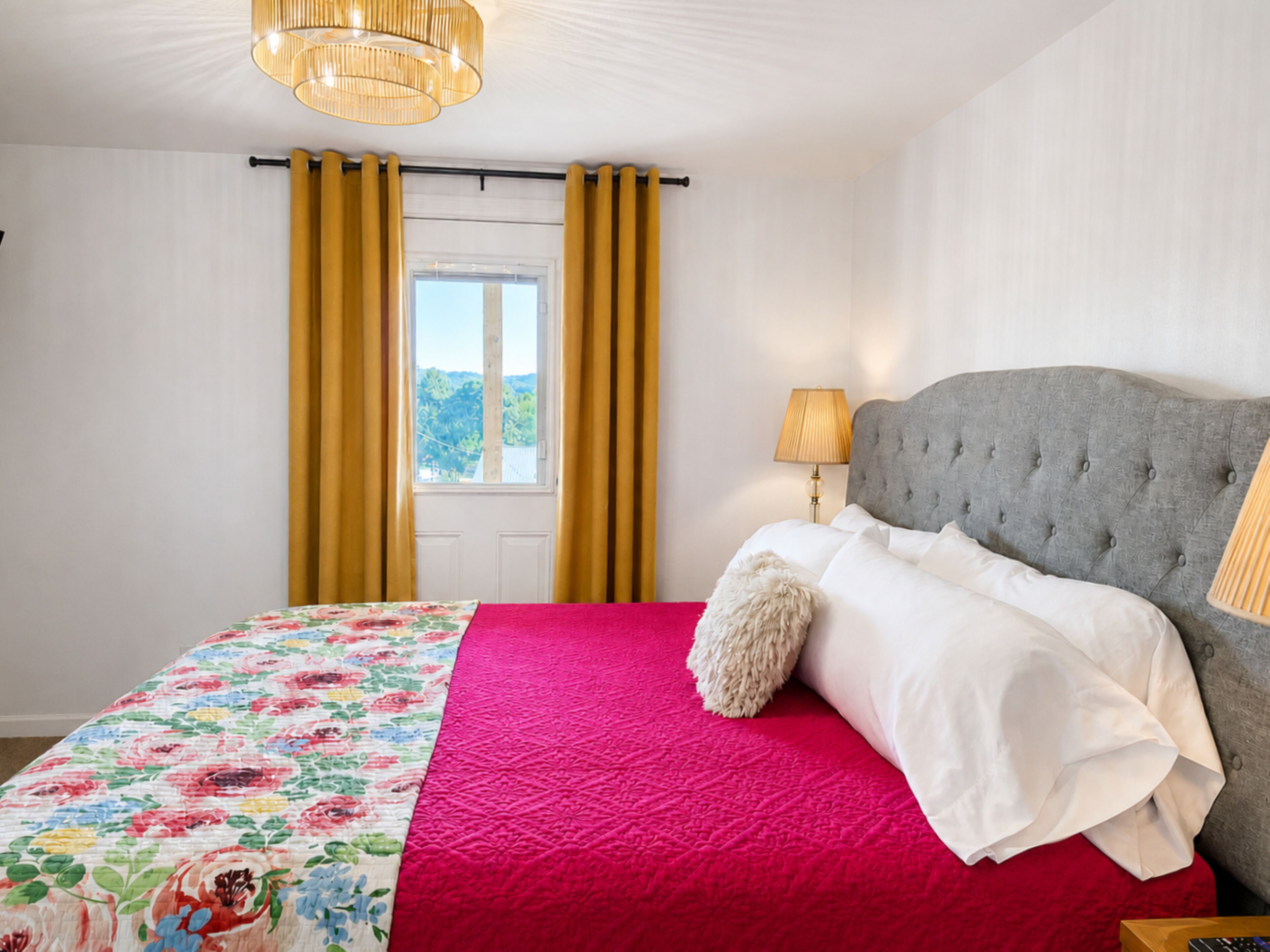 Una camera da letto con un letto, una finestra, tende, una lampada e vista sull'esterno.