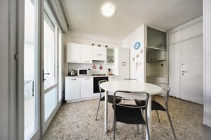 A compact kitchen with white cabinets, a microwave, and a round dining table with chairs. - Swiss Apartment, Jesolo (Lido di Jesolo)