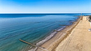 Una playa costera con un muelle que se adentra en el mar, un faro a lo lejos y un cielo despejado.