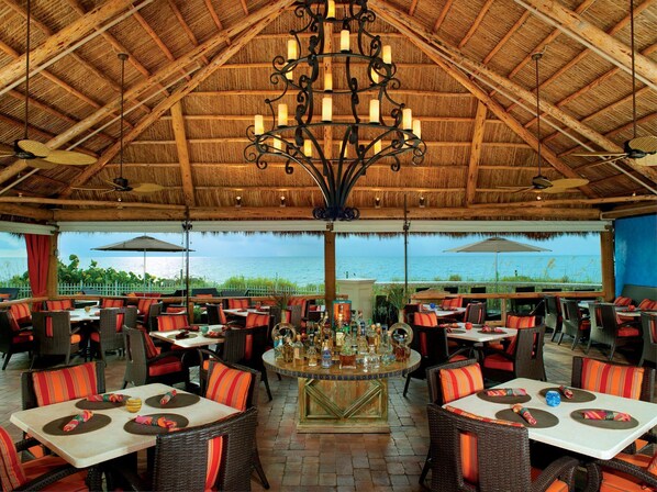 An outdoor dining area with wicker furniture, a central bar, and a view of the sea.