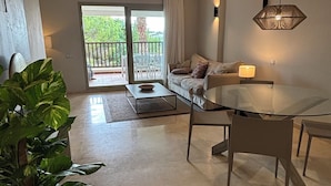 A modern living room with a glass dining table, a sofa, a coffee table, and a potted plant. - LAS COLINAS GOLF (Dehesa de Campoamor)