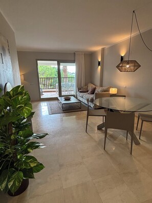 A modern living room with a glass dining table, a sofa, a coffee table, and a potted plant. - LAS COLINAS GOLF (Dehesa de Campoamor)