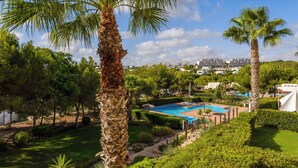 A pool surrounded by palm trees and greenery, with buildings in the background. - LAS COLINAS GOLF (Dehesa de Campoamor)
