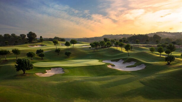 A golf course with sand bunkers, trees, and a sunset in the background. - LAS COLINAS GOLF (Dehesa de Campoamor)