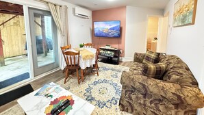 A living room with a sofa, a dining table with chairs, a TV mounted on the wall, and a sliding glass door leading to an outdoor area. - The Cozy Inn (Halifax)
