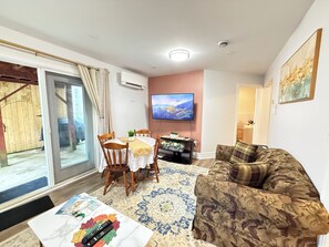 A living room with a sofa, a dining table with chairs, a TV mounted on the wall, and a sliding glass door leading to an outdoor area. - The Cozy Inn (Halifax)