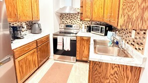 A modern kitchen with wooden cabinets, a stainless steel refrigerator, a stove, a microwave, and a sink. - The Cozy Inn (Halifax)
