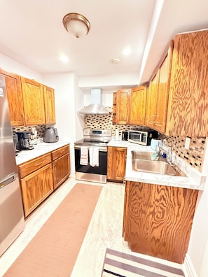 A modern kitchen with wooden cabinets, a stainless steel refrigerator, a stove, a microwave, and a sink. - The Cozy Inn (Halifax)