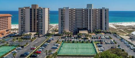 A high-rise hotel with multiple floors, a parking lot, and a tennis court.