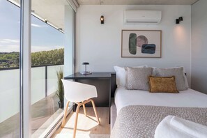 Ein modernes Schlafzimmer mit Bett, Nachttisch, Stuhl und Blick auf die Stadt.