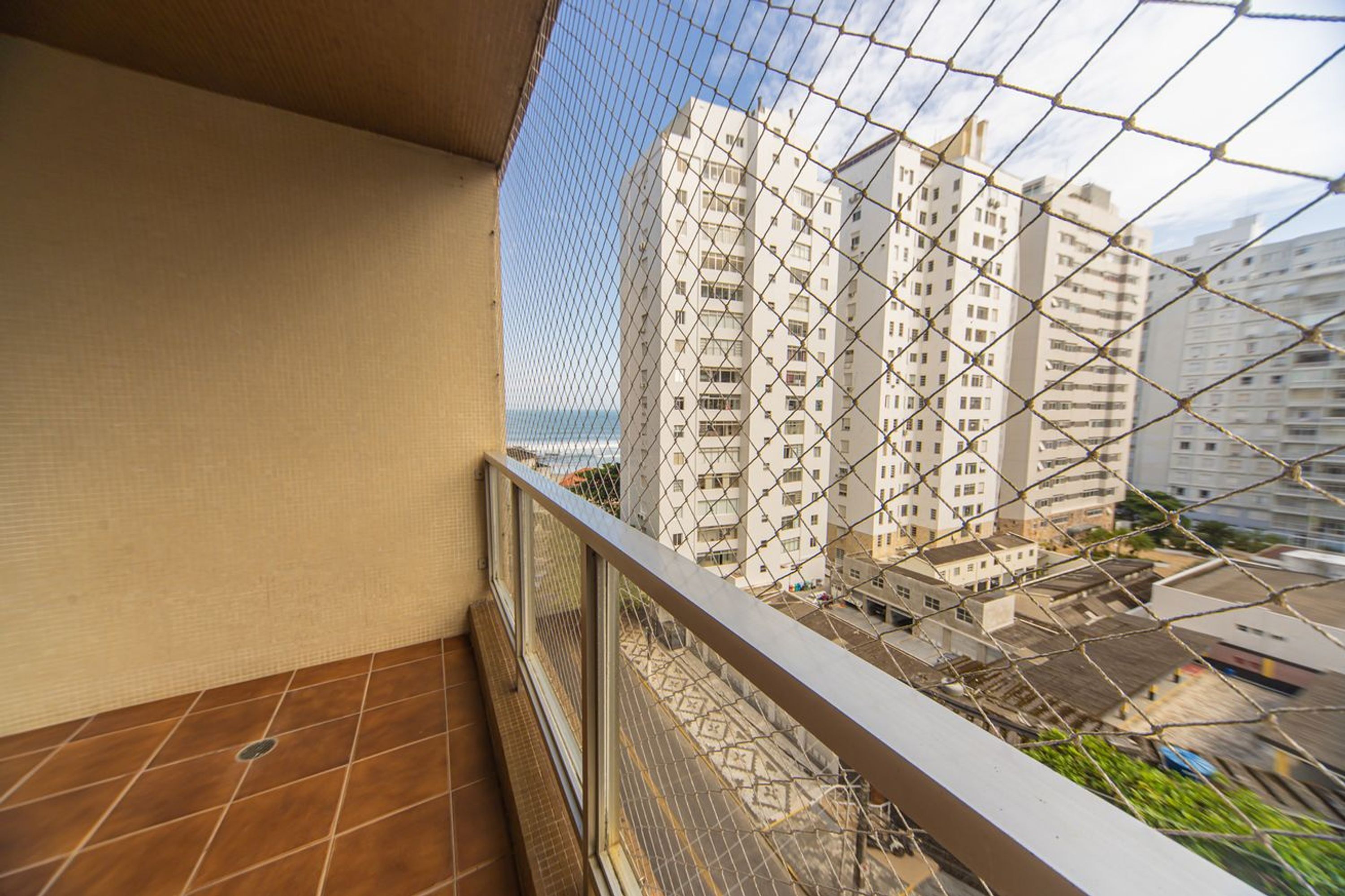 A balcony with a chain-link fence, a tiled floor, and a view of high-rise buildings and a body of water.