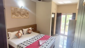 Quarto de hotel com cama, cabeceira, quadro na parede, porta e vista pela janela.