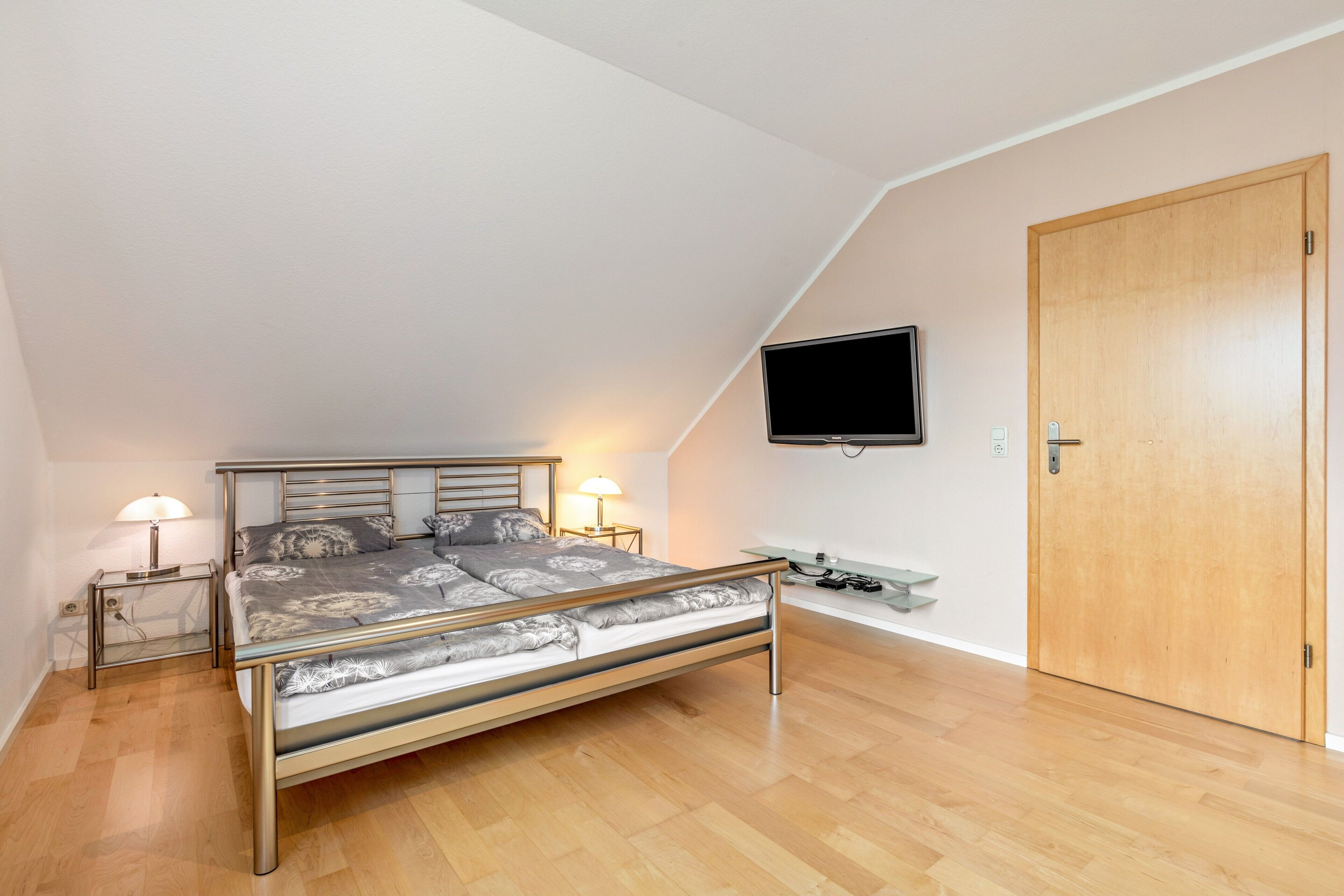 Ein Schlafzimmer mit einem Bett, Nachttischlampen, einem Fernseher, einer Holztür und einem kleinen Tisch.