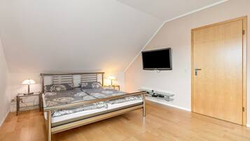 Ein Schlafzimmer mit einem Bett, Nachttischlampen, einem Fernseher, einer Holztür und einem kleinen Tisch.