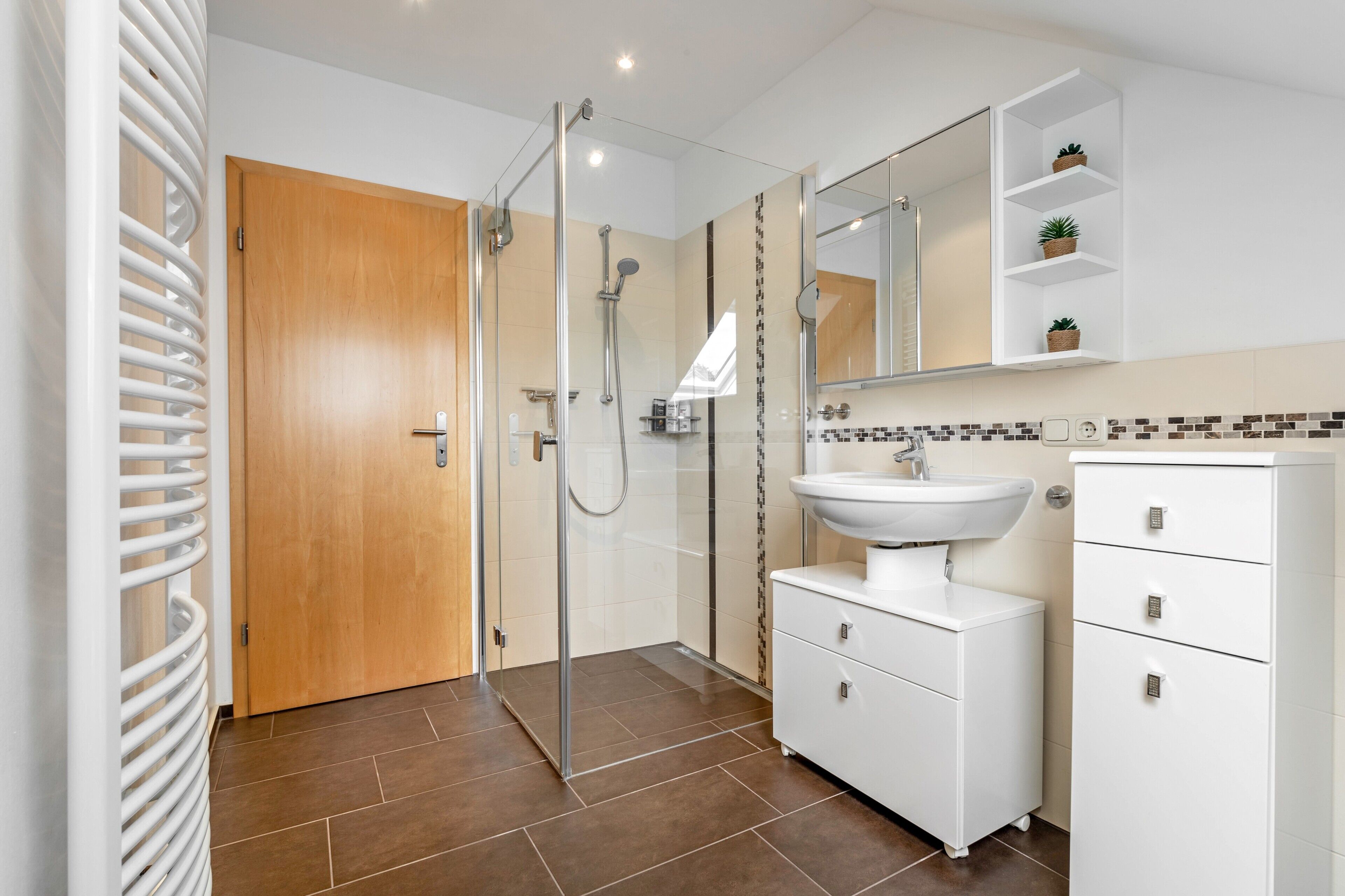 A modern bathroom with a glass shower enclosure, a white sink, and a wooden door.