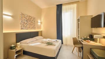 A hotel room with a bed, desk, chair, TV, and artwork on the wall.