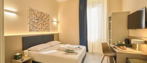 Habitación de hotel con cama, escritorio, silla, televisor y una obra de arte en la pared.