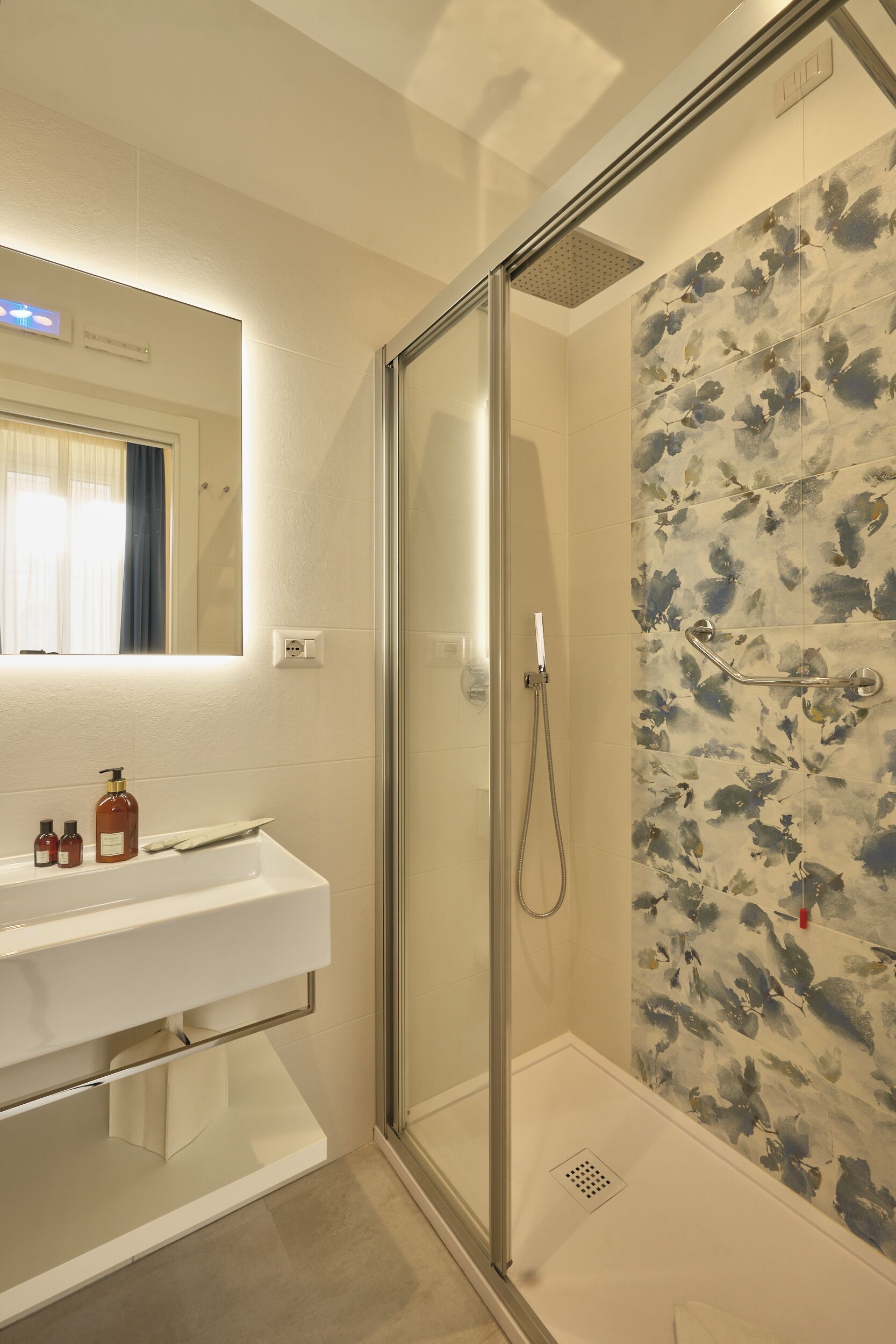 Une salle de bain moderne avec une douche à parois de verre, un lavabo blanc avec des articles de toilette et un miroir au-dessus.