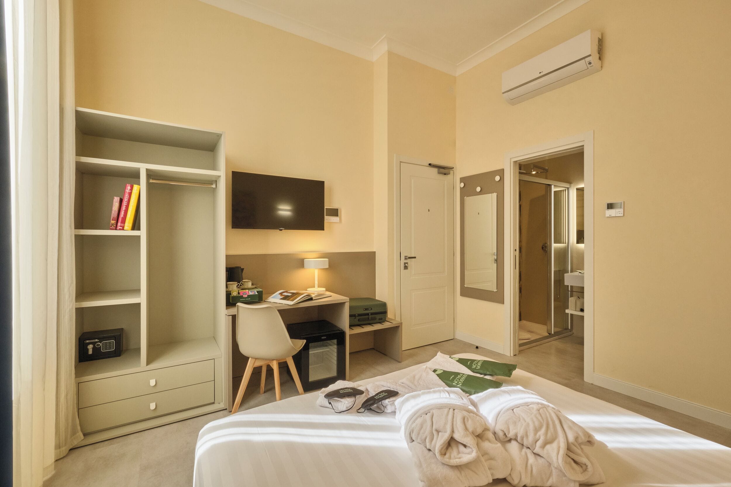 Una habitación de hotel con una cama, un escritorio con silla, un armario, un televisor y un baño visible a través de una puerta abierta.