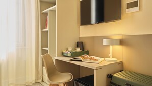 A compact hotel room with a desk, chair, TV, lamp, and a suitcase. - Rishon (Rome)