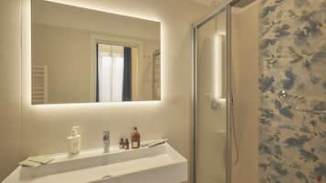 A bathroom with a white sink, a mirror, and a shower with floral tiles.