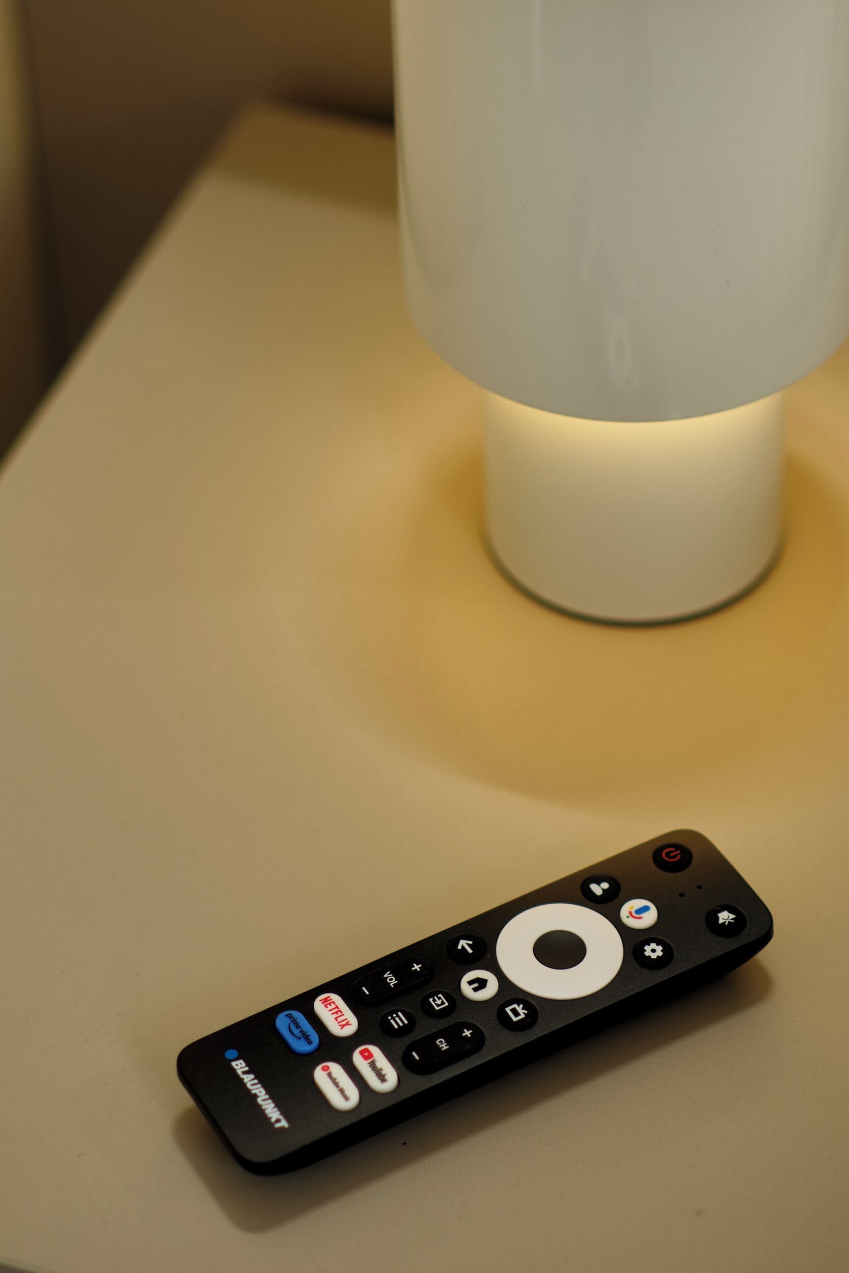 A remote control with a circular button and a brand name on a flat surface.