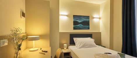 Una habitación de hotel con cama, mesita de noche, lámpara, jarrón con flores y un cuadro en la pared.