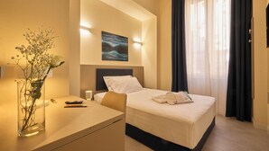 A hotel room with a bed, bedside table, lamp, and a painting on the wall. - Rishon (Rome)