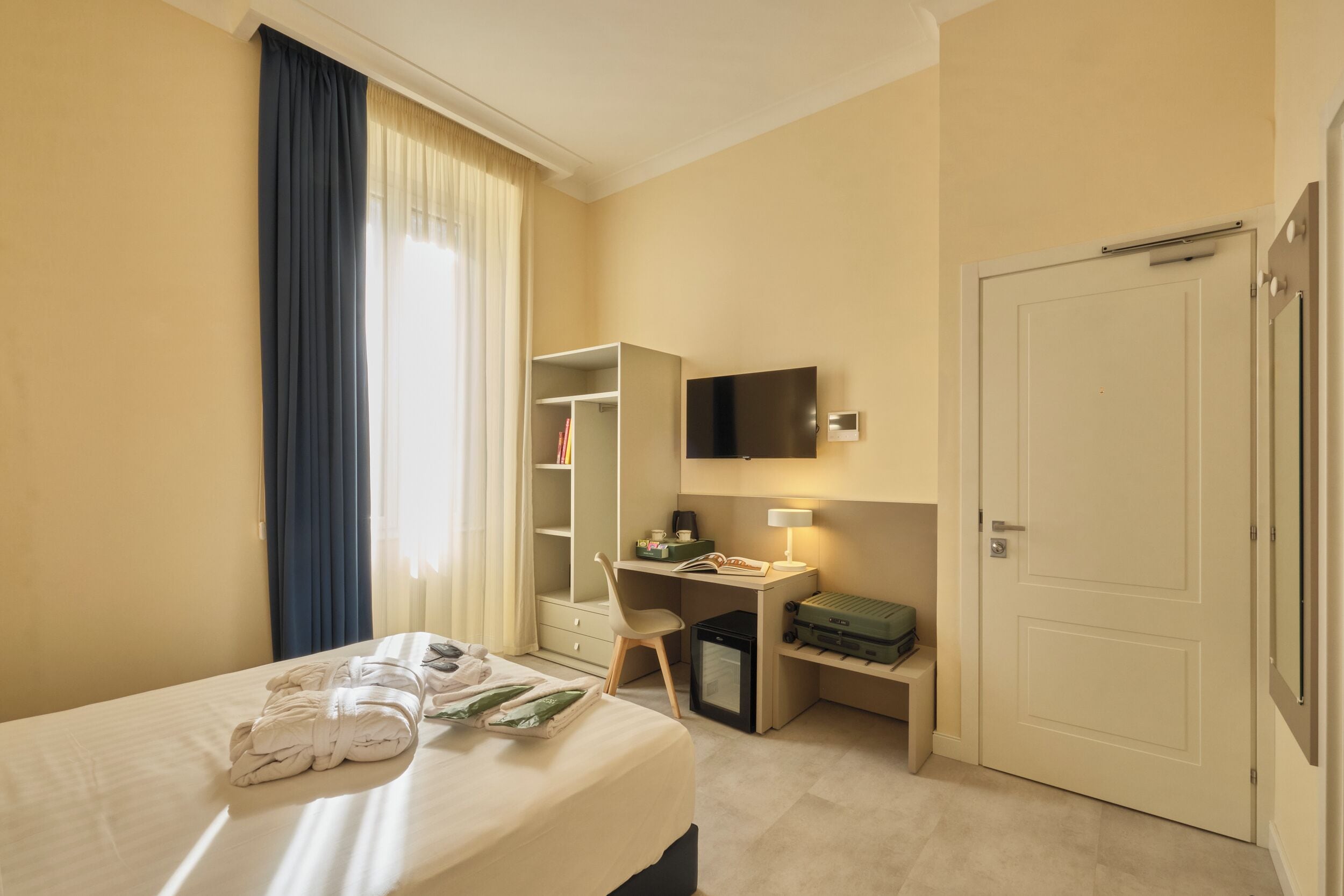 A hotel room with a bed, a desk, a chair, a wardrobe, a television, and a door.