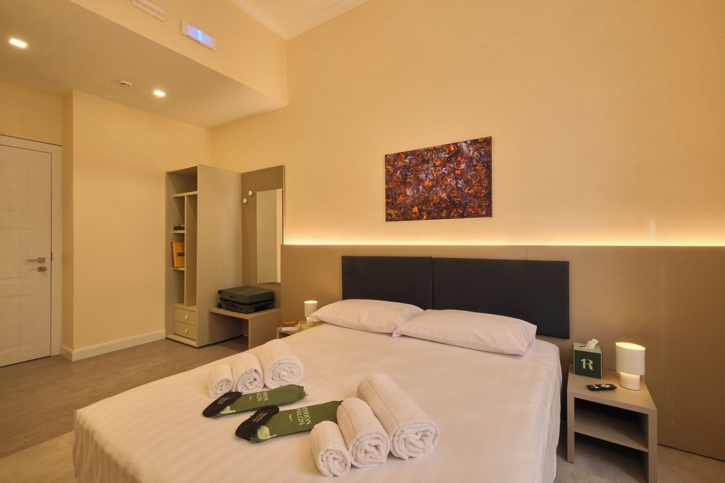 A hotel room with a bed, a bedside table with a lamp, a nightstand with a lamp, a painting on the wall, and a closet with a mirror.