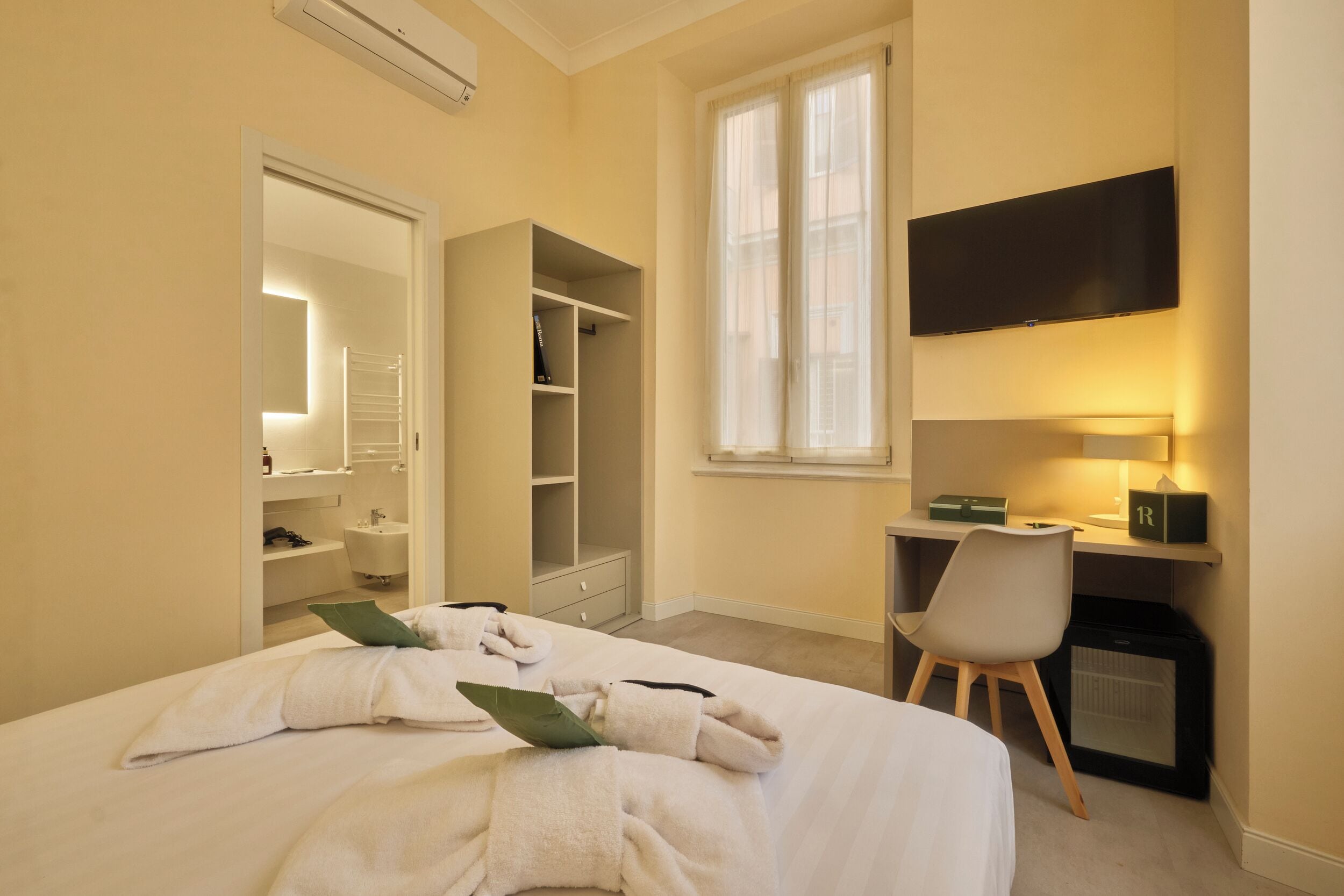 Una habitación de hotel con cama, escritorio, silla, televisor y armario.