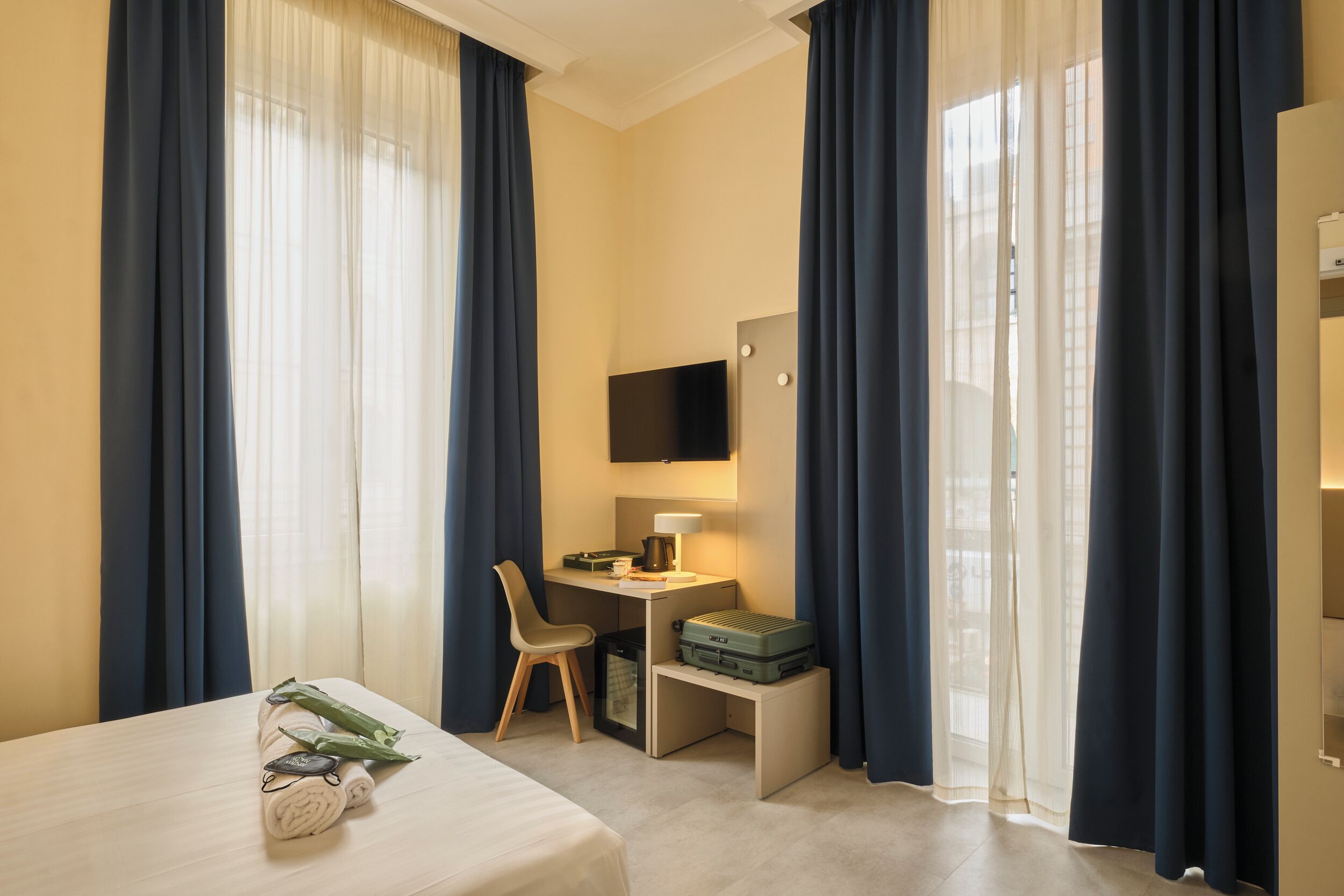 Een hotelkamer met een bed, een bureau met stoel, een televisie en een koffer op een bankje.