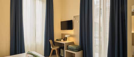 A hotel room with a bed, a desk with a chair, a television, and a suitcase on a bench.