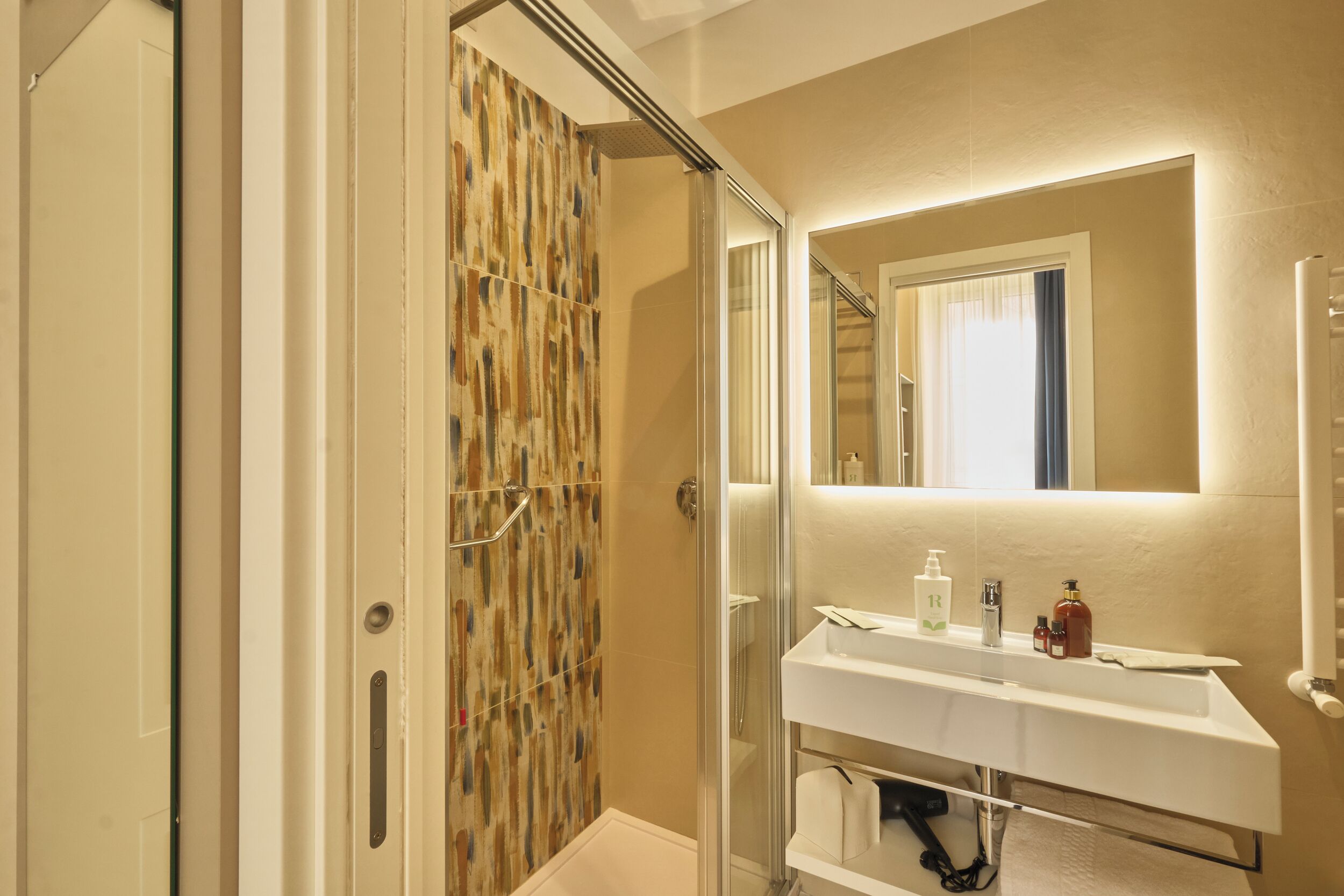A modern bathroom with a glass shower enclosure, a white sink, and a mirror above the sink.
