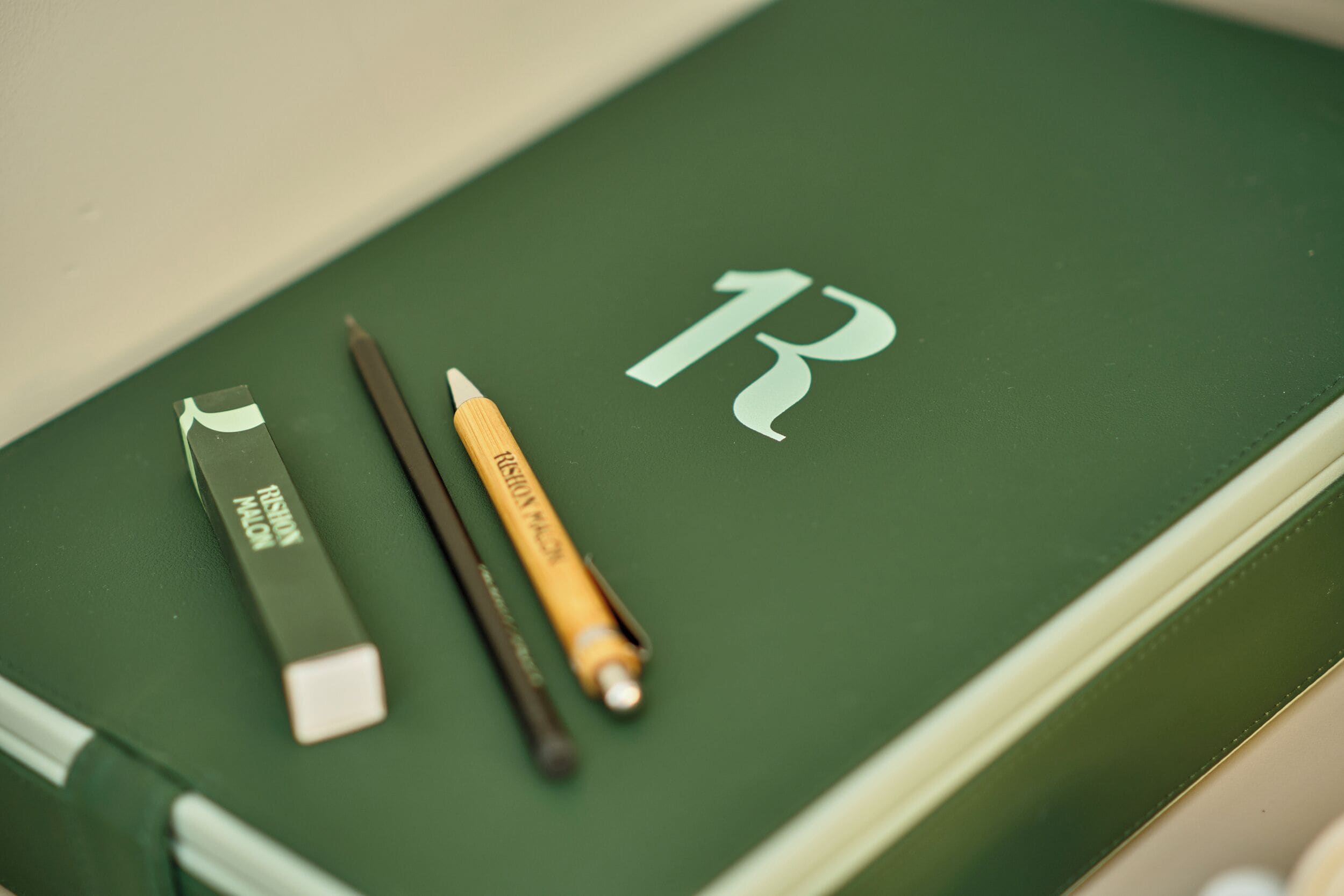 Un livre vert avec un grand «R» blanc sur la couverture, un stylo noir et un crayon noir et blanc.