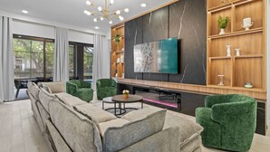 Ein modernes Wohnzimmer mit einem Ecksofa, grünen Sessel, einem Couchtisch, einem Flachbildfernseher und einer Holzwandregal mit Dekorationselementen.