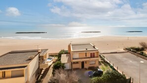 Vista costera con playa, zona de estacionamiento y un edificio de techo plano con una pequeña piscina.