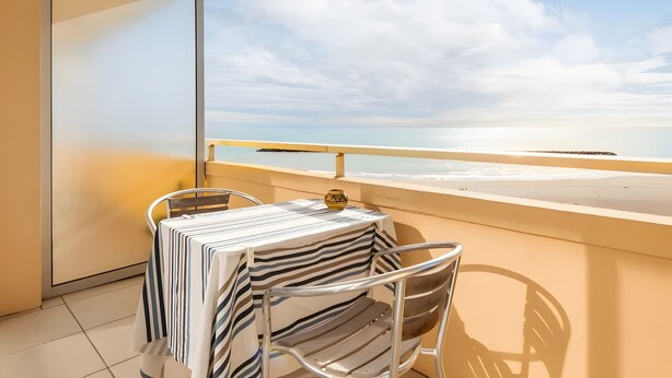 Un balcón con una mesa para dos, con vista a una playa bajo un cielo despejado.