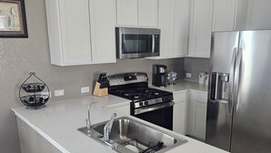 Una cocina moderna con armarios blancos, electrodomésticos de acero inoxidable, microondas integrado y refrigerador de acero inoxidable.