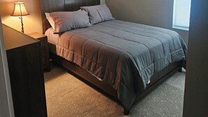 Un dormitorio con cama, mesita de noche, lámpara y dos cuadros colgados en la pared.